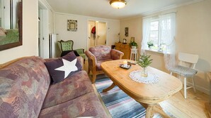 A cozy living room with a patterned sofa, a wooden coffee table with a candle and decorative items, and a window with sheer curtains. - 3 bedroom gorgeous home in överlida (Överlida)