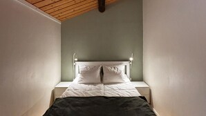 Una habitación pequeña y estrecha con techo inclinado y una cama con ropa blanca.