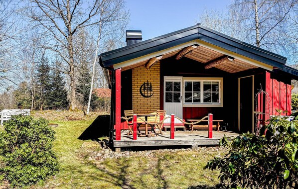 A small cabin with a wooden deck, a red door, and a window.