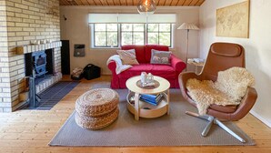 Una sala de estar acogedora con chimenea de ladrillo, un sofá rojo, un sillón marrón y una mesa de centro redonda.