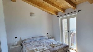 A bedroom with a wooden ceiling, a bed with a white headboard, a nightstand, and a window with a view.