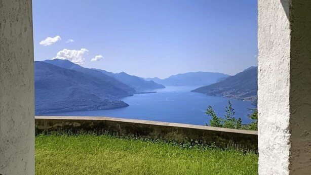 A view of a lake with mountains in the background, viewed from a balcony with a concrete ledge.