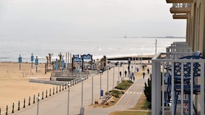 A beach promenade with a clear view of the ocean, a pedestrian walkway, and a building with balconies.