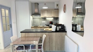 A modern kitchen with a wooden island, white chairs, and a dining table. - L'appartement Pins D97 (CAPBRETON)