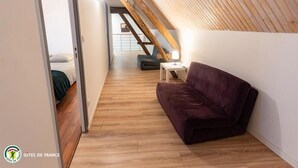 Un dormitorio estilo loft moderno con techo inclinado de madera, un sofá morado y una pequeña mesa con lámpara.