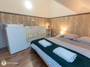 Cozy retreat with a single bed, bedside table, and crib, set amidst a tree-patterned wallpaper and wooden floor.
