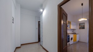 A hallway leading to a kitchen with a washing machine, cabinets, and a hanging light fixture.