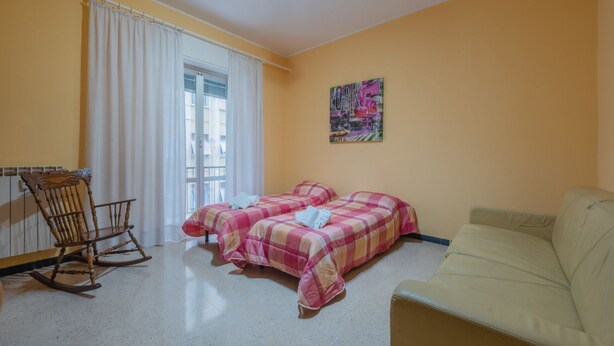 A room with two beds, a rocking chair, a sofa, and a window with curtains.