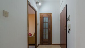 A narrow hallway with a wooden door at the end, a light switch on the wall, and a telephone on the right.
