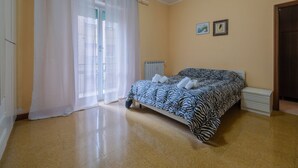 A bedroom with a bed, curtains, a radiator, and a small bedside table.