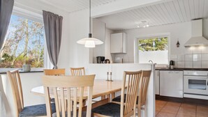 Eine moderne Küche mit weißen Schränken, einem Esstisch mit Stühlen und einem großen Fenster mit Vorhängen.