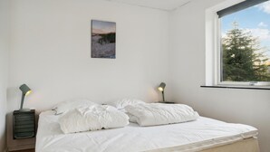 Ein Schlafzimmer mit einem Bett, zwei Nachttischen mit Lampen, einem Fenster mit Blick auf Bäume und einem Bild an der Wand.