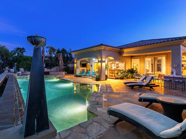 Un espace piscine comprenant des chaises longues, une pergola et une terrasse bien éclairée.