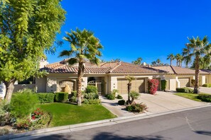 A residential house with a tiled roof, a garage, and a well-maintained lawn with various plants and flowers.