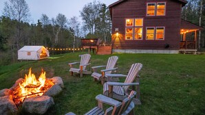 Une cabane avec un foyer et des chaises Adirondack dans la cour.