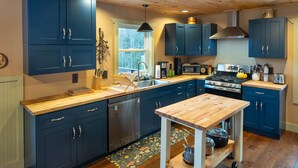 Une cuisine moderne avec des meubles de couleur bleu foncé, un plan de travail en bois, un lave-vaisselle encastré, une cuisinière et une petite table sur laquelle se trouve une casserole.