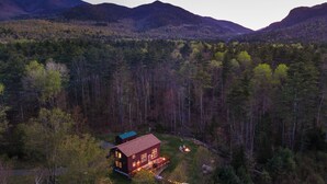 Une cabane dotée d’une terrasse et d’un espace extérieur aménagé, le tout entouré de montagnes boisées.