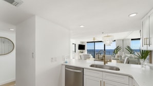 Een moderne keuken met witte kastjes, een roestvrijstalen vaatwasser en een groot raam met uitzicht op de oceaan.