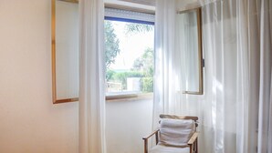 Una habitación con una silla cerca de una ventana, una cama con un edredón colorido y un espejo en la pared.