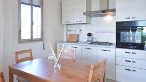 Una cocina moderna con armarios blancos, estufa a gas, horno y ventana con persianas.
