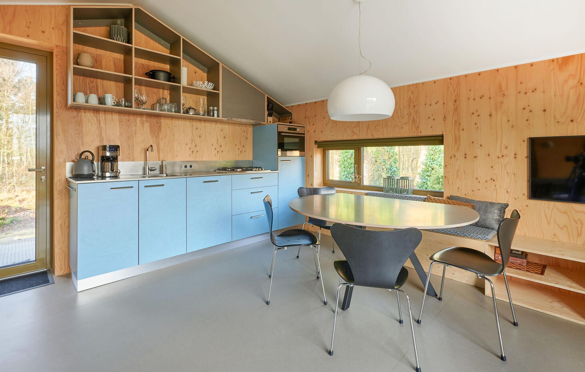 Une cuisine moderne avec des meubles de rangement bleus, une table de salle à manger ronde et une grande fenêtre.