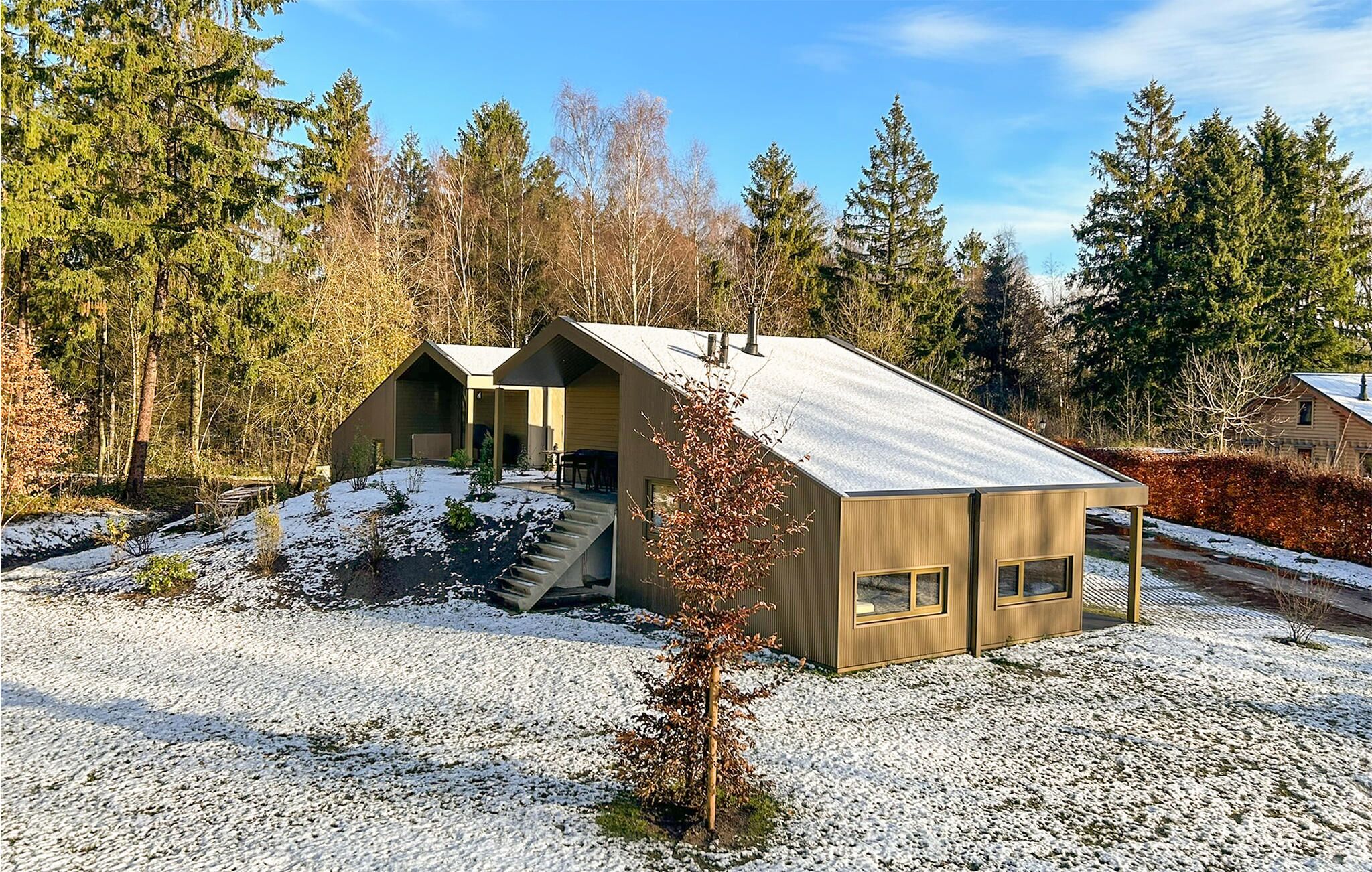 A modern cabin with a sloped roof, a small porch, and a gravel driveway.