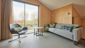 A modern room with a large window, a grey sofa with patterned cushions, a black chair, and a small round table.