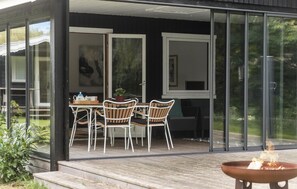 A modern outdoor dining area with a glass enclosure, wooden deck, and a fire pit. - Cozy home in Gilleleje with kitchen (Gilleleje)