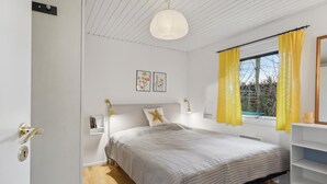 A bedroom with a bed, bedside lamps, a window with yellow curtains, a wall-mounted shelf, and a framed picture above the bed. - Cozy home in Gilleleje with kitchen (Gilleleje)