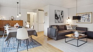 A modern living room with a dining area, featuring a sofa, coffee table, and dining table with chairs. - Cozy home in Gilleleje with kitchen (Gilleleje)