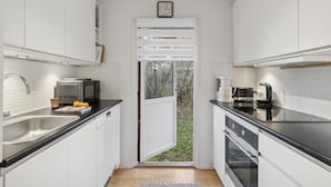 A modern kitchen with white cabinets, a black countertop, a built-in oven, a coffee maker, and a microwave. - Cozy home in Gilleleje with kitchen (Gilleleje)