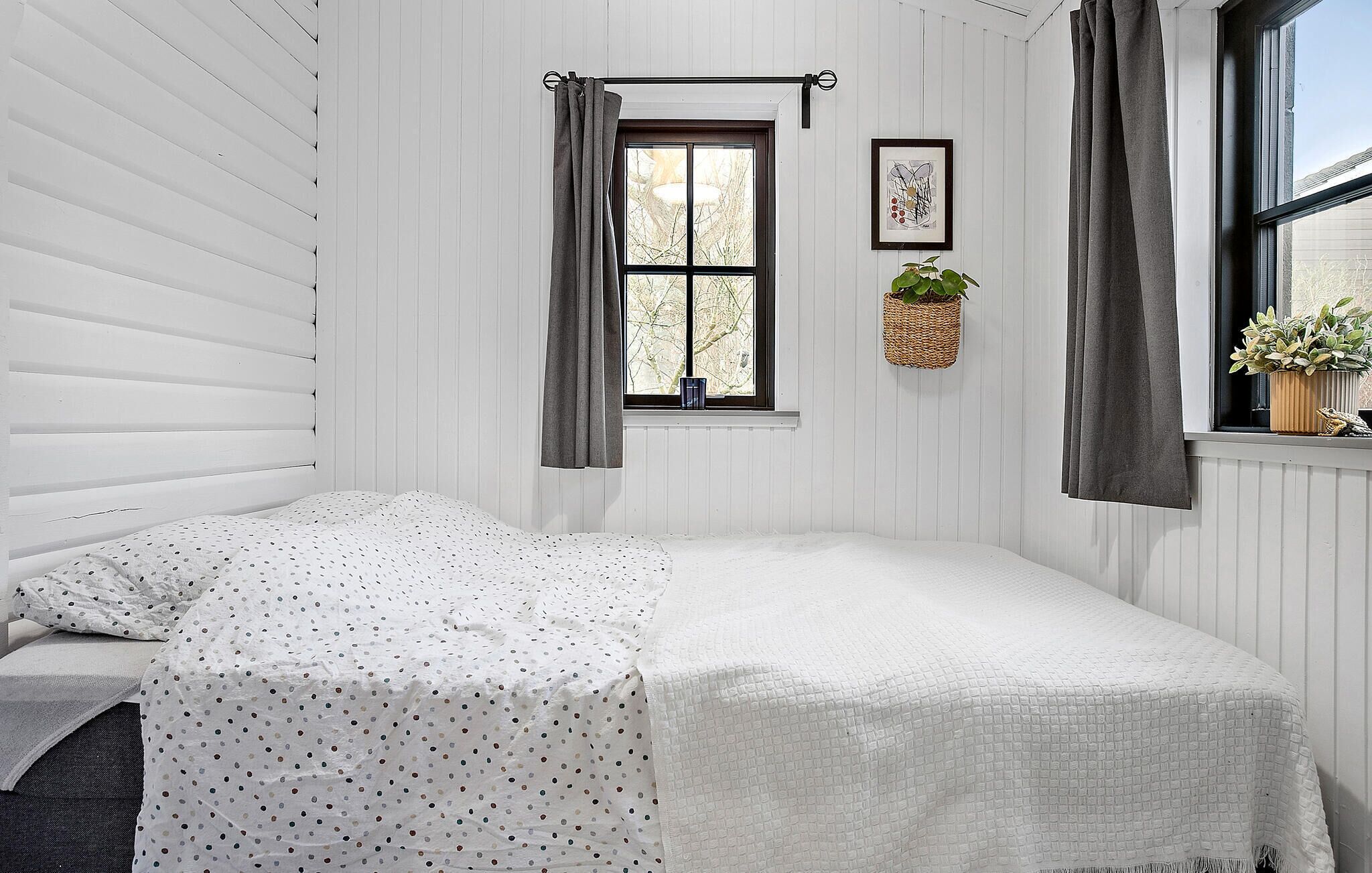 Een slaapkamer met een bed, een raam met gordijnen, een aan de muur bevestigde plant en een lijst met een foto.