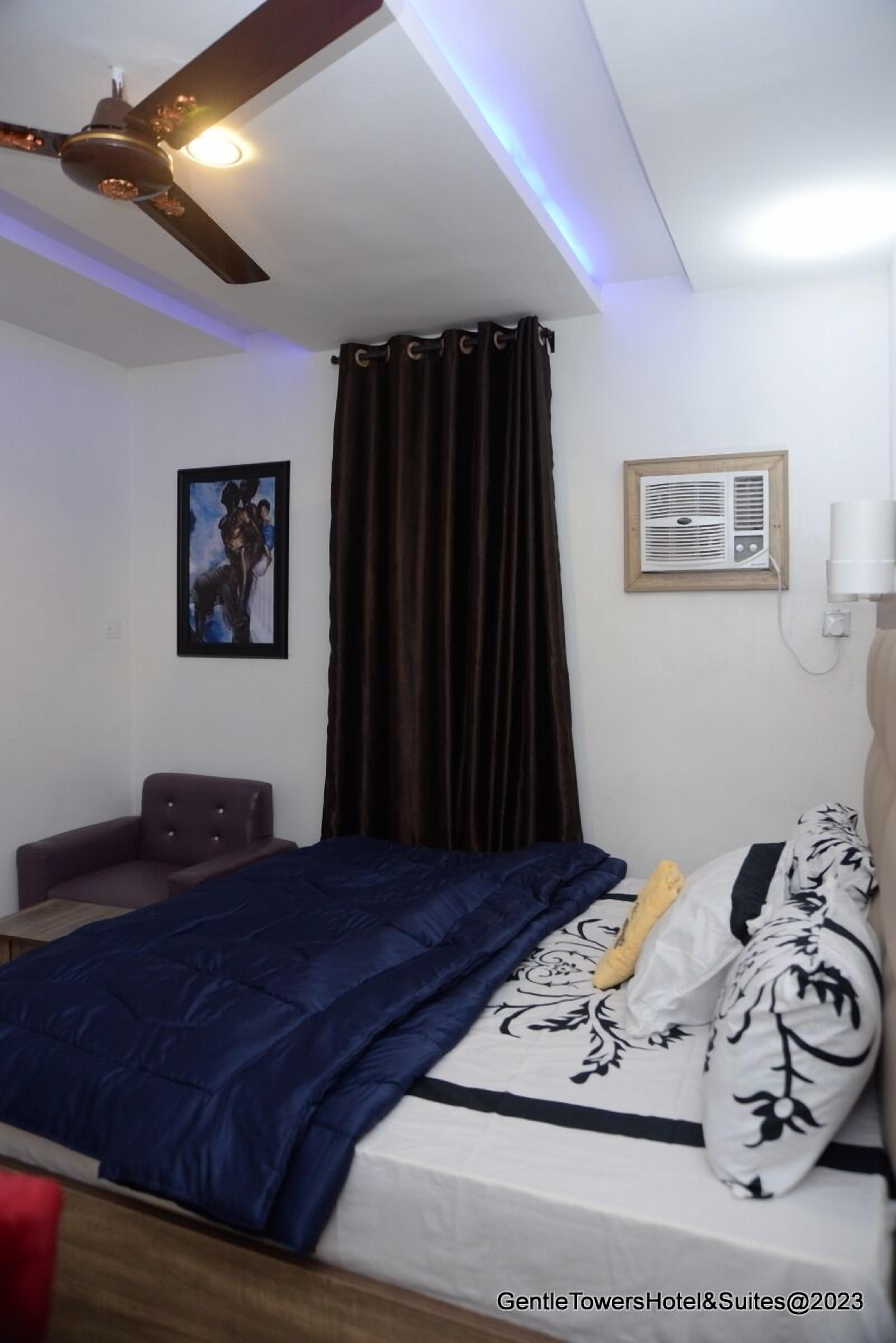 Un dormitorio con cama, ventilador de techo, aire acondicionado de pared y un cuadro enmarcado.