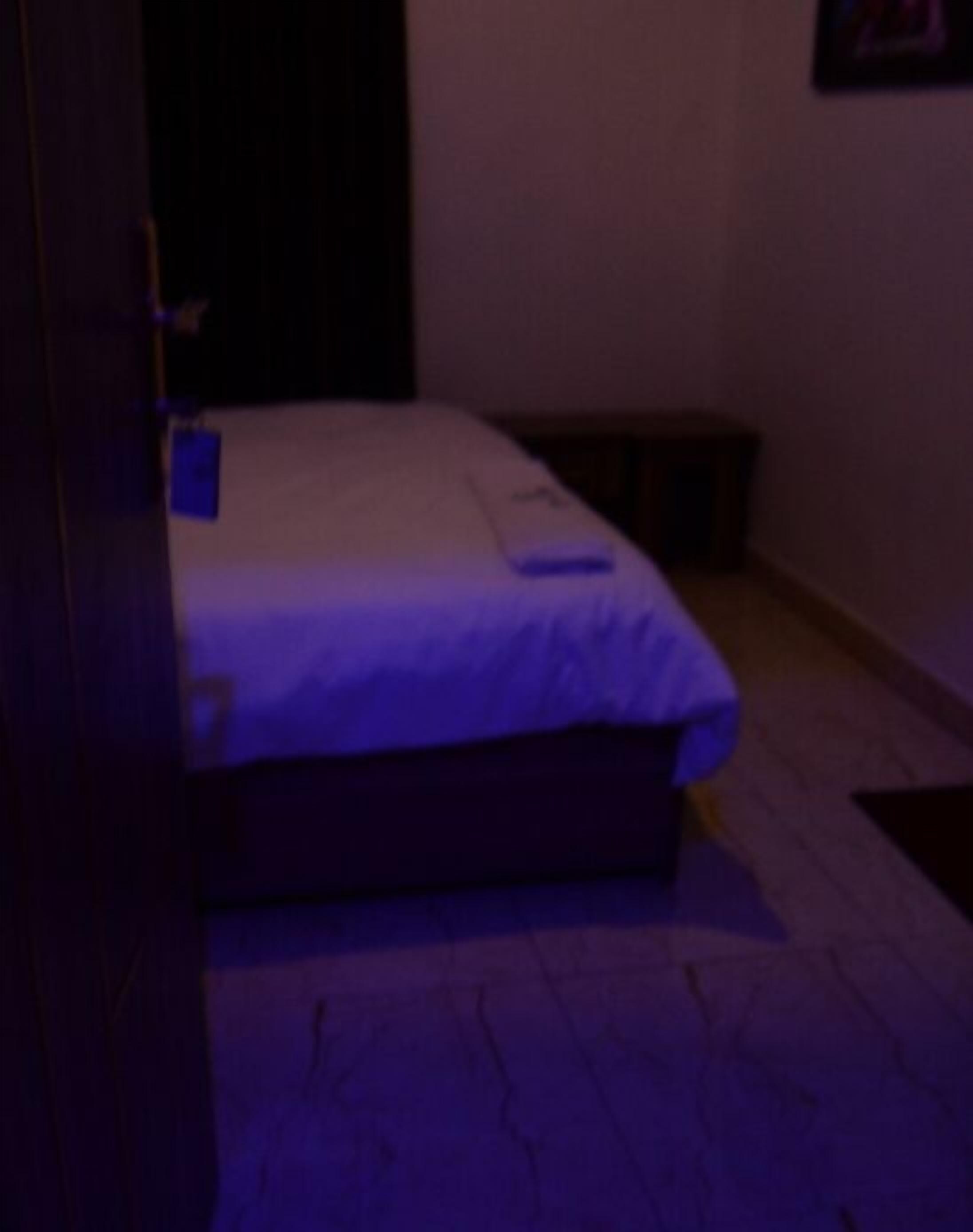 Ein Zimmer mit einem Bett, einem kleinen Tisch und einem an der Wand befestigten Regal.