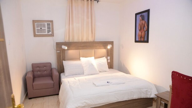 A bedroom with a bed, a chair, a small table, and a wall-mounted air conditioner. - gentle tower hotels (Lagos)