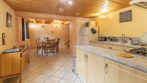 A cozy kitchen with wooden cabinets, a dining area with a table and chairs, and a small refrigerator. - LA Piemontaise - LE Penatsot (AUSSOIS)