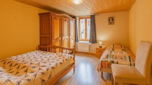 A bedroom with two beds, a wooden wardrobe, a window with curtains, and a lamp on a bedside table. - LA Piemontaise - LE Penatsot (AUSSOIS)