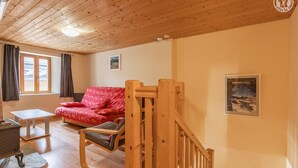 A cozy room with a wooden ceiling, a red sofa, a small table, and a staircase. - LA Piemontaise - LE Penatsot (AUSSOIS)