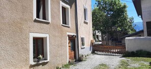 A narrow cobblestone street flanked by buildings with small windows and doors, some with potted plants. - LA Piemontaise - LE Tsozal (AUSSOIS)