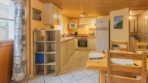 A cozy kitchen with wooden cabinets, a dining table with chairs, and a window with patterned curtains. - LA Piemontaise - LE Tsozal (AUSSOIS)