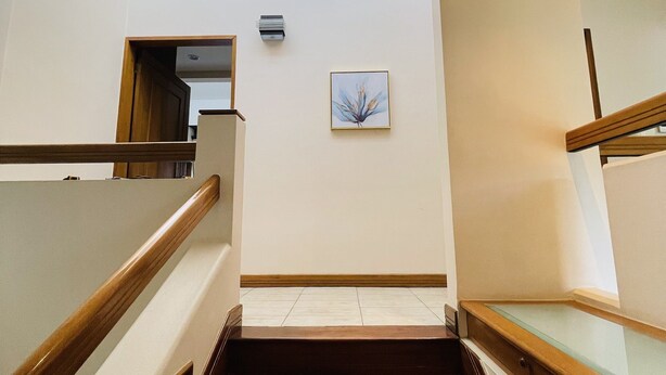 A staircase with wooden handrails and a glass balustrade, leading to a landing with a wall-mounted air conditioning unit and a framed picture. - The Rainier Bed & Breakfast (San José)