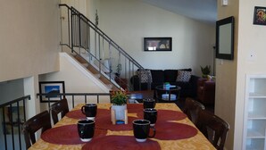 A dining area with a table set for four, a staircase, and a living room in the background.