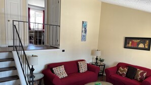 A living room with a staircase, two red sofas, a glass coffee table, and a small side table with a lamp.
