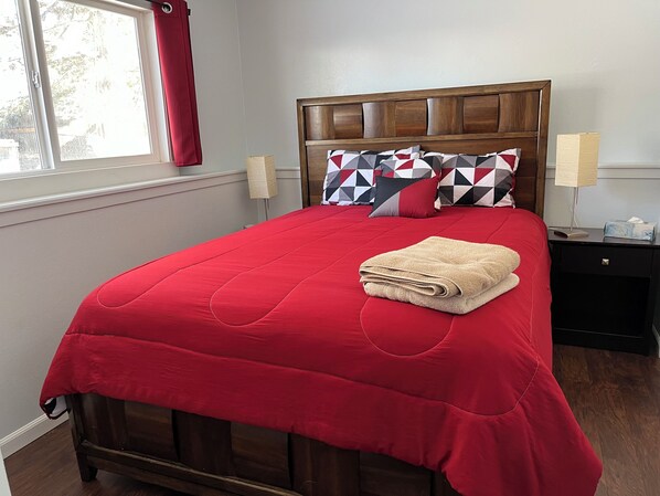 A neatly made bed with a red bedspread, a folded beige towel, and geometric patterned pillows. - Cozy, pet friendly, home. Great location for walks, food, Boulder, Lyons & RMNP (Longmont)