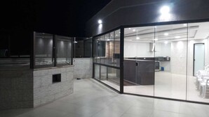 Un bâtiment moderne doté d’une façade en verre, avec un espace cuisine visible à travers le verre et un sol carrelé.