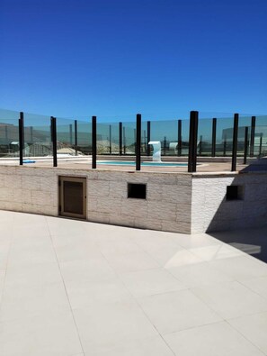 Eine Dachterrasse mit Swimmingpool, einer Steinmauer und wolkenlosem, blauem Himmel.