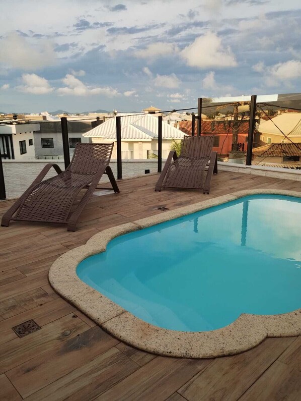 A rooftop pool with two lounge chairs and a view of the cityscape.
