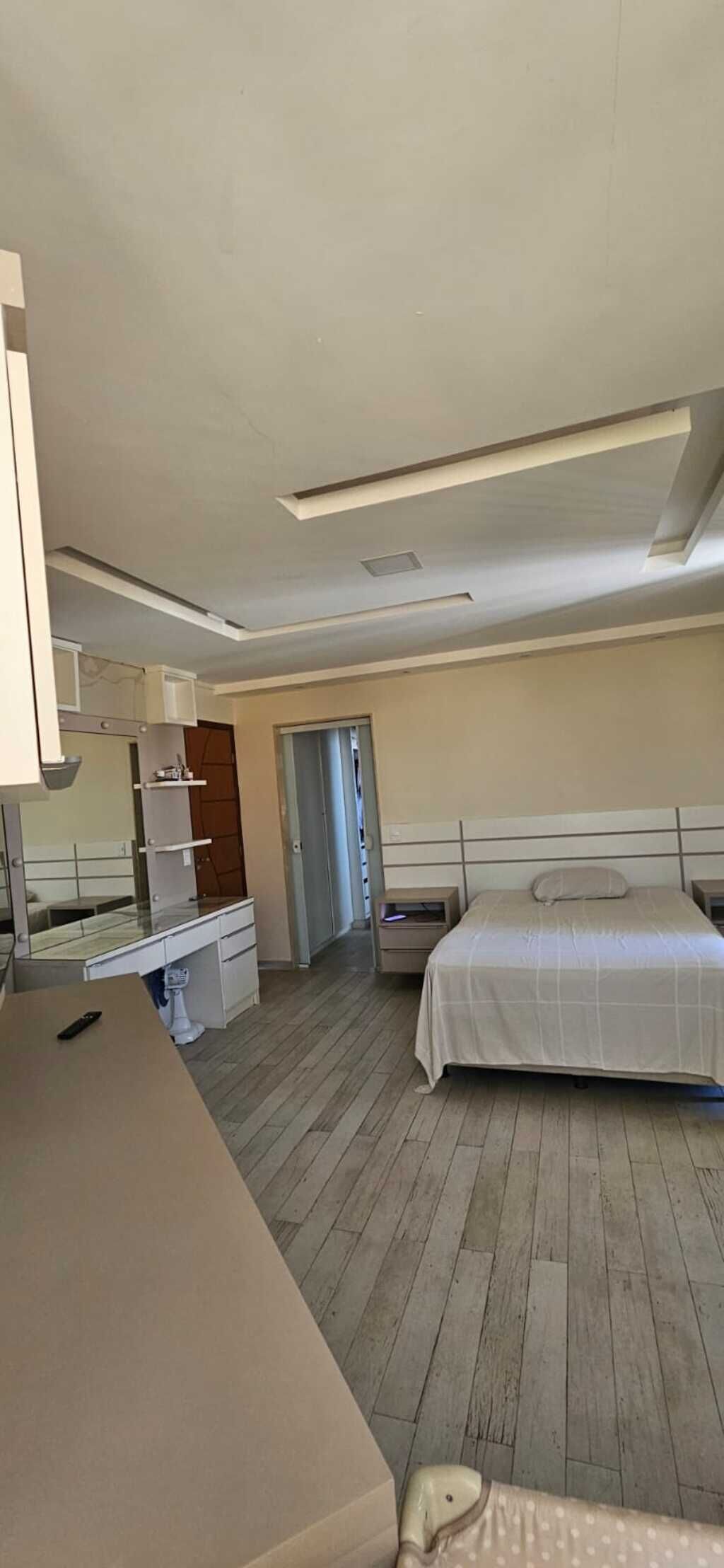 A hotel room with a bed, a desk, a chair, a small table, a mirror, and a door.