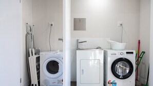 Une buanderie équipée de deux machines à laver à chargement frontal, d’un petit meuble de rangement et d’une serpillière posée sur le sol.