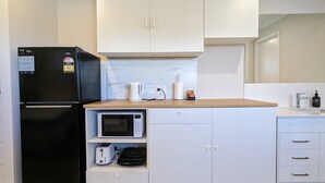 Une cuisine compacte avec des meubles blancs, un réfrigérateur noir, un four à micro-ondes et une machine à café.
